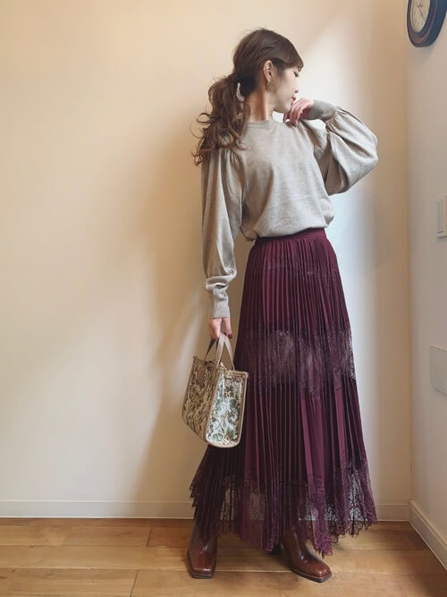 赤のプリーツスカート×ベージュのニット×ブラウンのブーツ×ベージュのバッグ