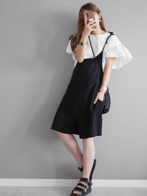 ショートパンツのサロペット×白のフリルブラウス×黒のサンダル×黒のプリーツバッグ