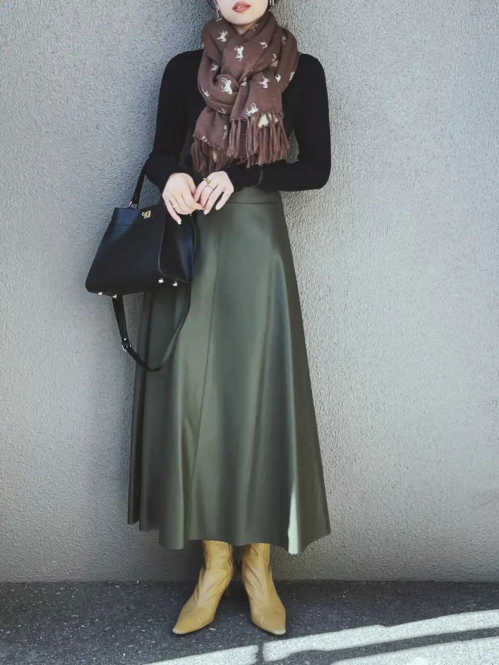 緑のフレアスカート×黒のニット×ブラウンのマフラー×ベージュのショートブーツ×黒のレザーのバッグ