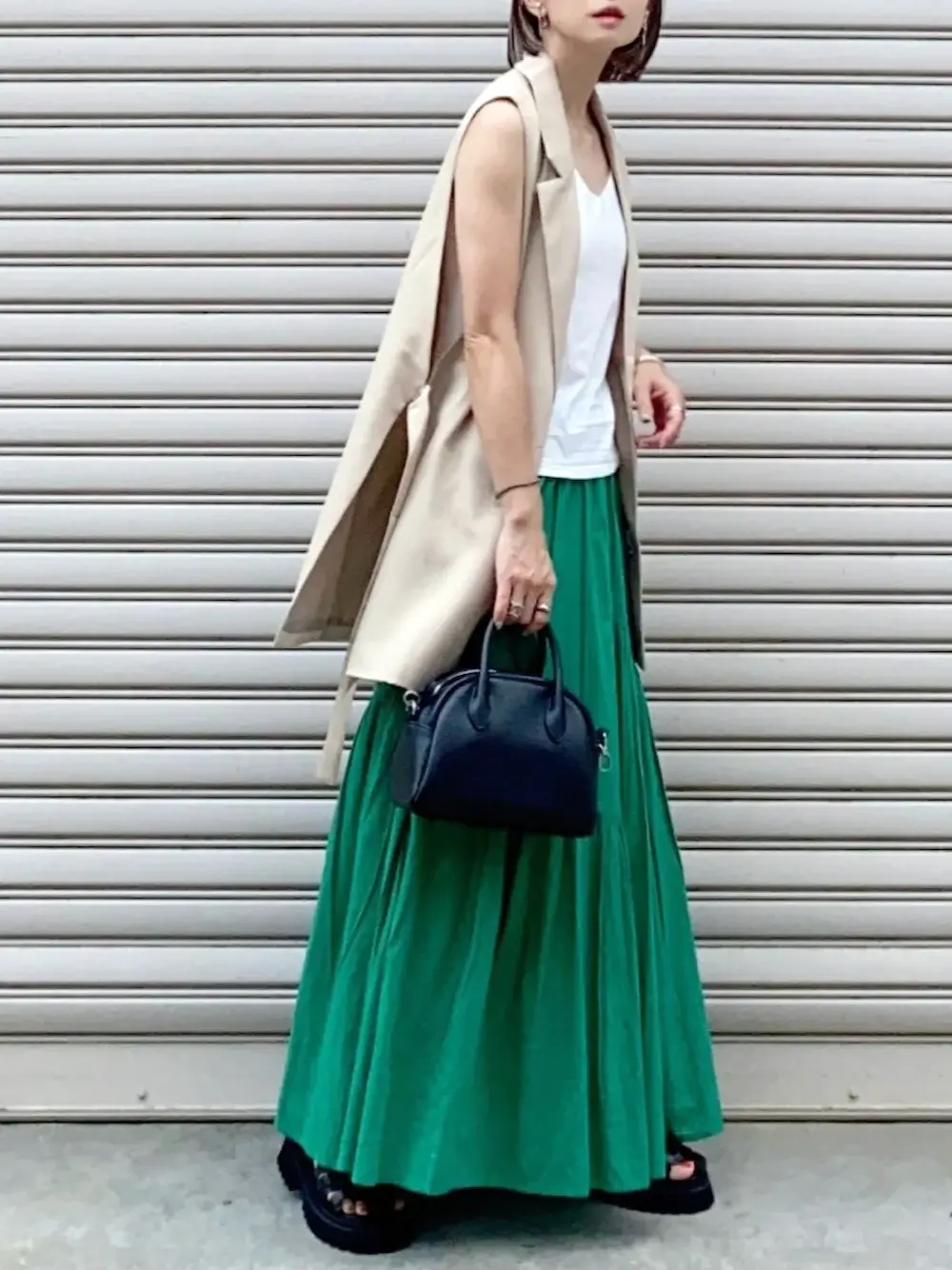 緑のフレアスカート×白のタンクトップ×ベージュのベスト×黒の厚底サンダル×黒のミニバッグ