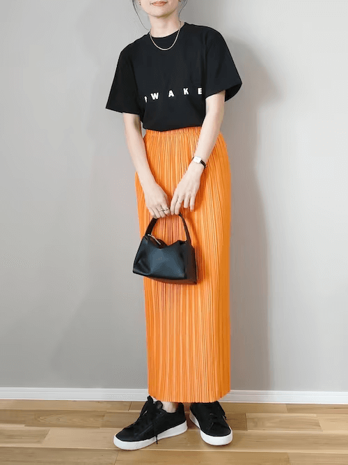 黒Tシャツ×オレンジのプリーツスカート×黒のスニーカー