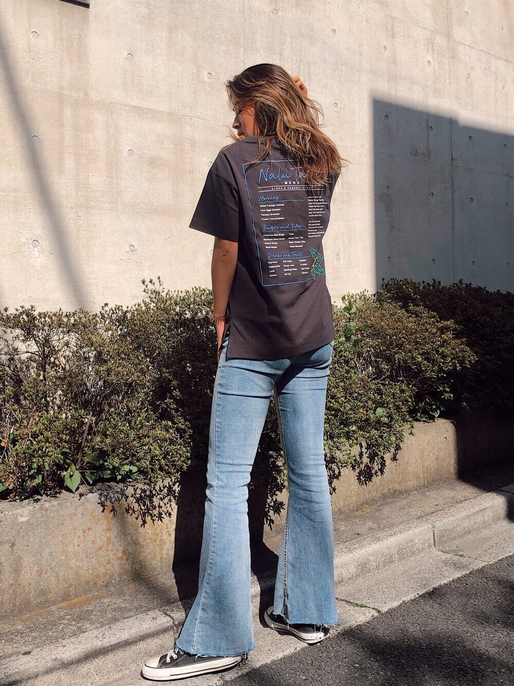 グレーの刺繍Tシャツ×フレアデニム×黒のスニーカーのサーフ系ファッション
